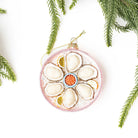 Decorative ornament resembling an oyster with a red coral center, hanging on a white background with greenery.
