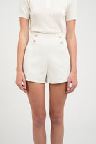 White shorts with gold buttons worn by a person on a white background