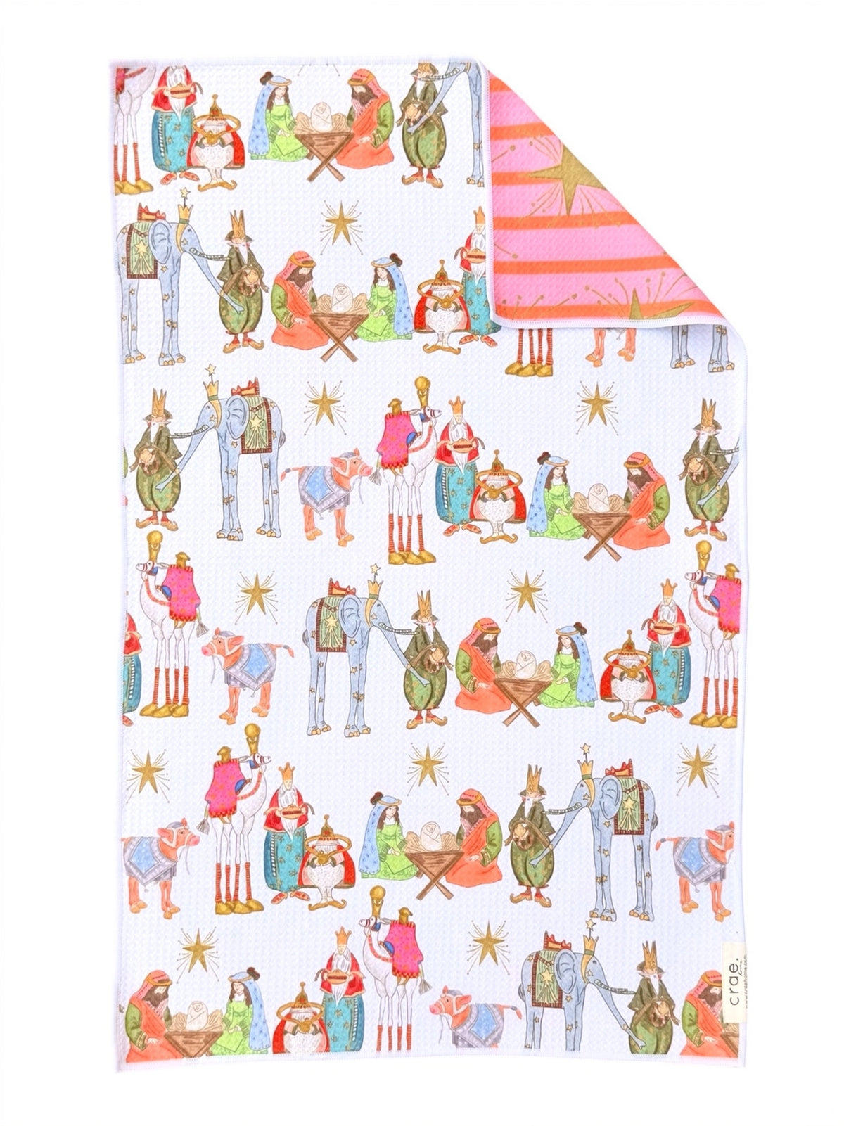 A white fabric towel, featuring a colorful cartoon pattern of Christmas characters around a manger. The top right corner is folded over to show the reverse side, which has a pink and orange striped pattern with a gold star.