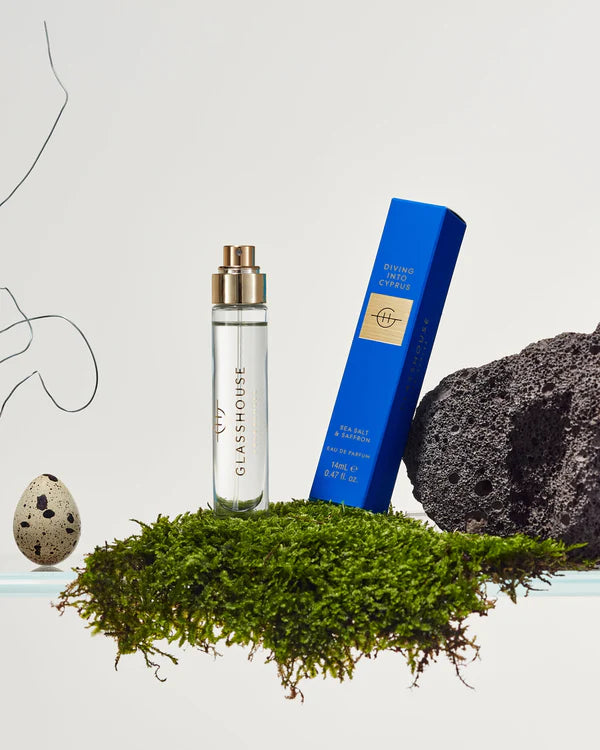 Glasshouse perfume bottle, blue box, and decorative stones on a white background