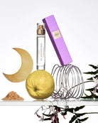 Glasshouse perfume bottle with purple cap, lemon, moon-shaped object, and floral elements on a white background
