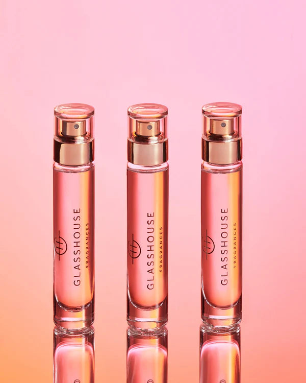 Three glass perfume bottles with rose gold caps on a gradient pink and orange background.
