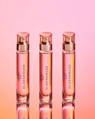 Three glass perfume bottles with rose gold caps on a gradient pink and orange background.