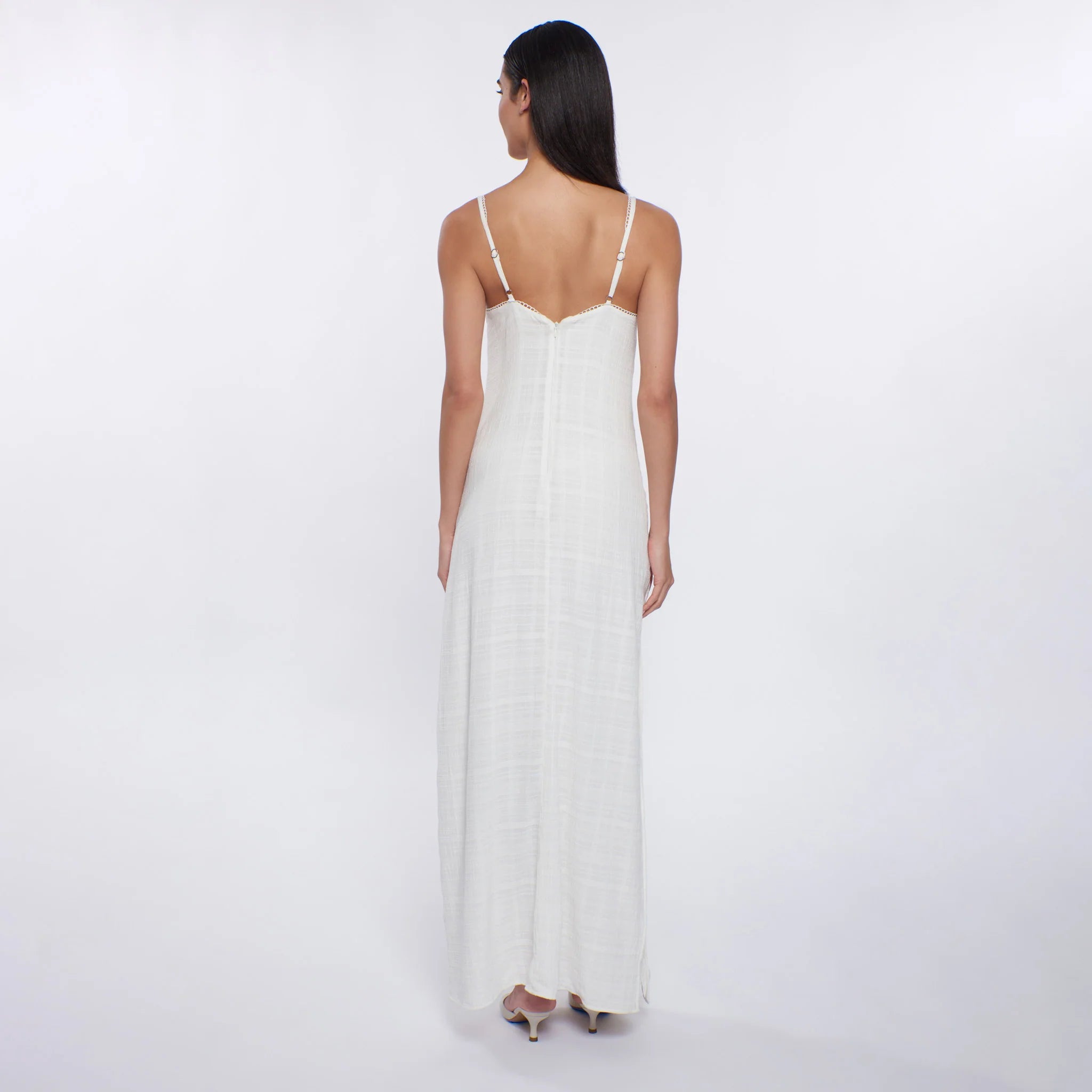 Woman wearing a white dress with thin straps on a plain background
