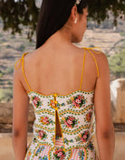 Woman wearing a floral dress with yellow straps, standing outdoors with a scenic background.