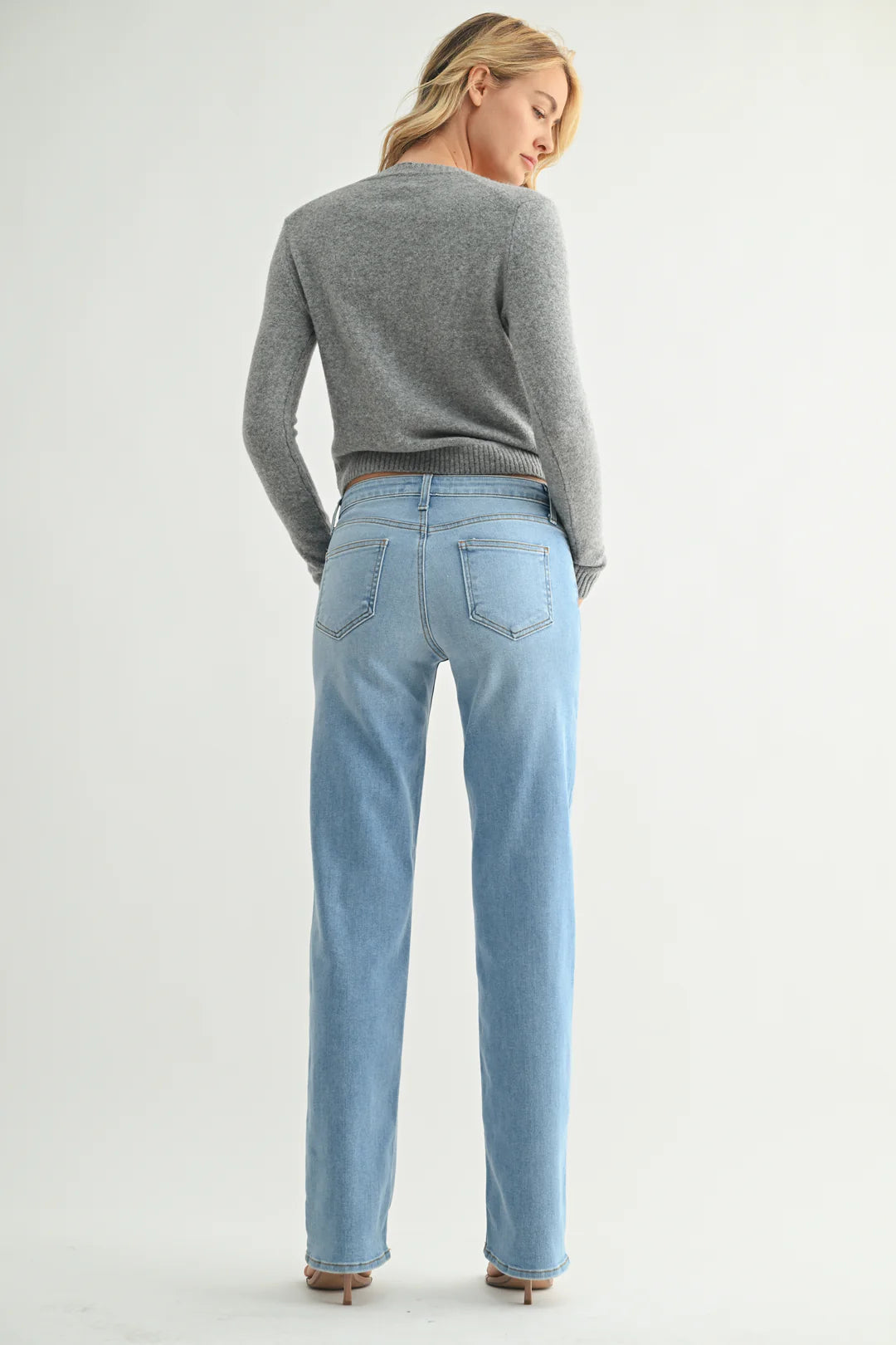 Woman wearing a gray sweater and light blue jeans on a white background