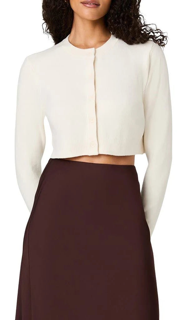 A woman wearing a cream long-sleeve cropped cardigan with a button-front closure and a dark brown skirt, shown against a plain white background.