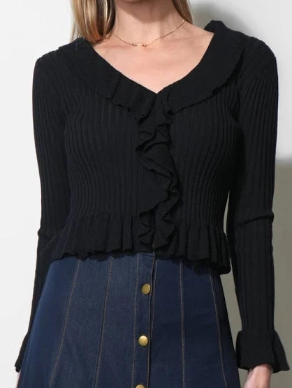 A woman wearing a black ribbed long-sleeve top with a ruffled V-neckline and ruffle detail down the front, paired with a dark blue denim skirt.