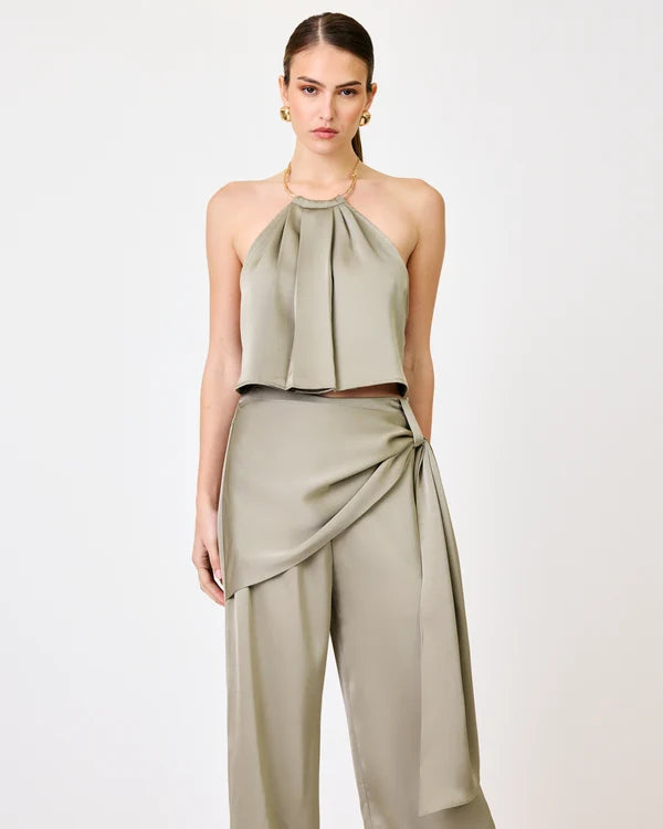 A model wearing a two-piece sage green outfit consisting of a halter-neck crop top and matching draped wide-leg pants, shot against a plain white studio background.