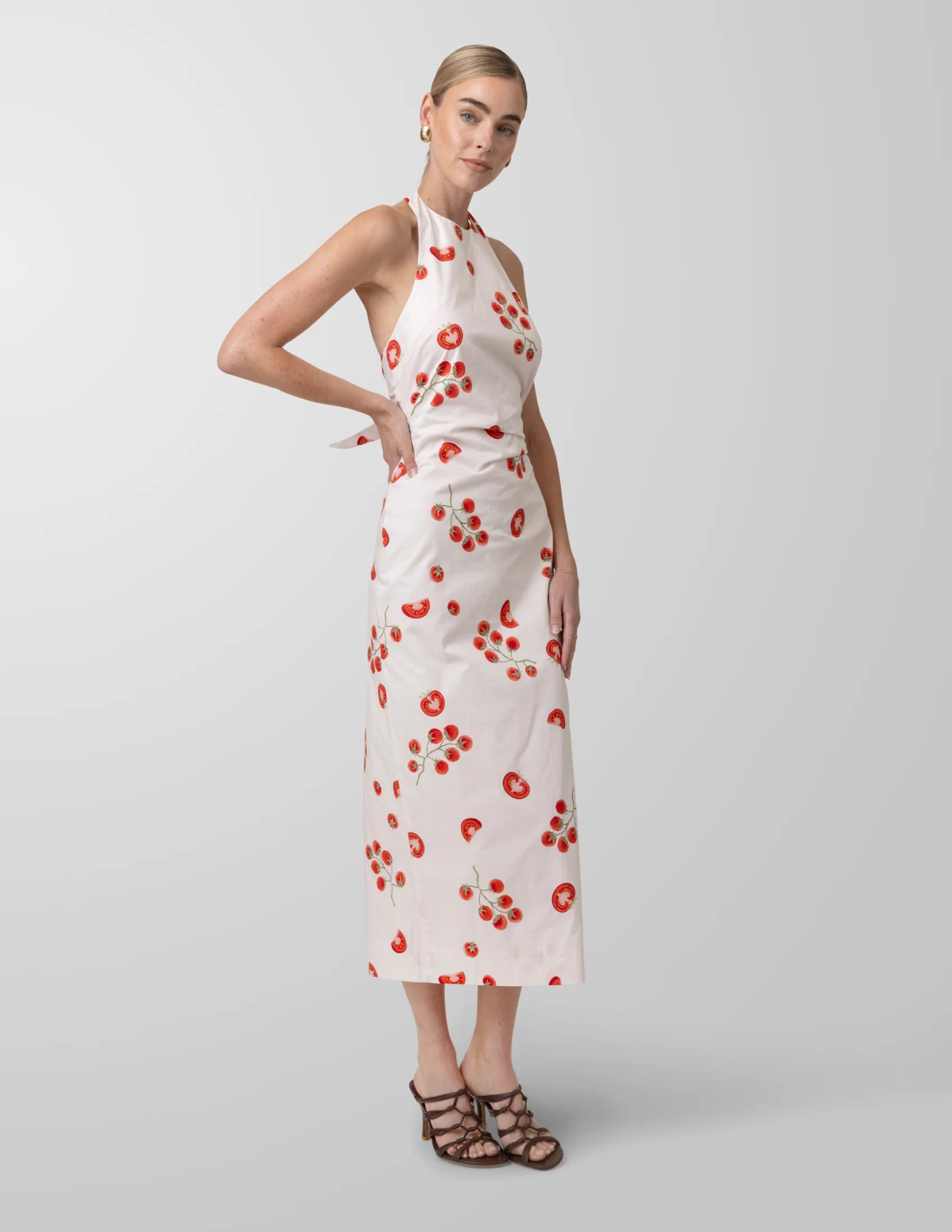 Woman wearing a white dress with red tomato patterns on a light gray background