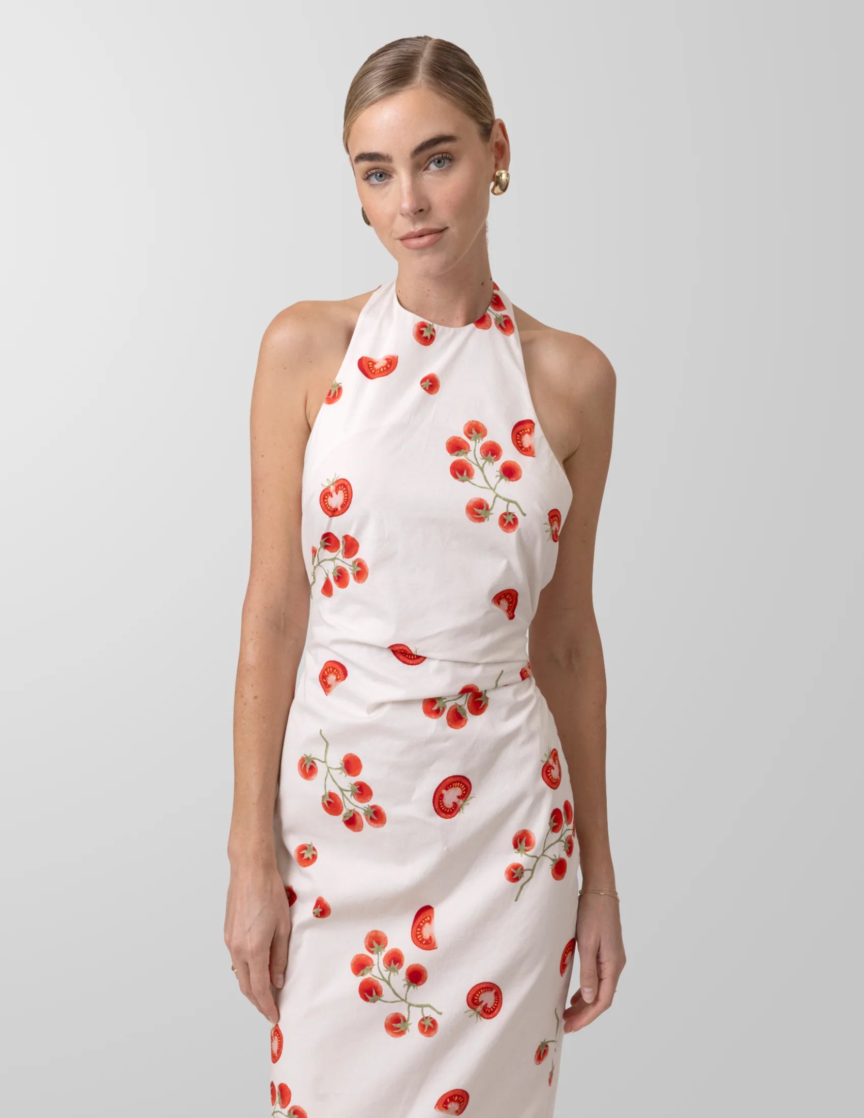 Woman wearing a white dress with red tomato vine patterns on a plain background