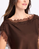 A close-up of a woman wearing a brown satin top with a wide off-the-shoulder neckline and sheer lace trim.